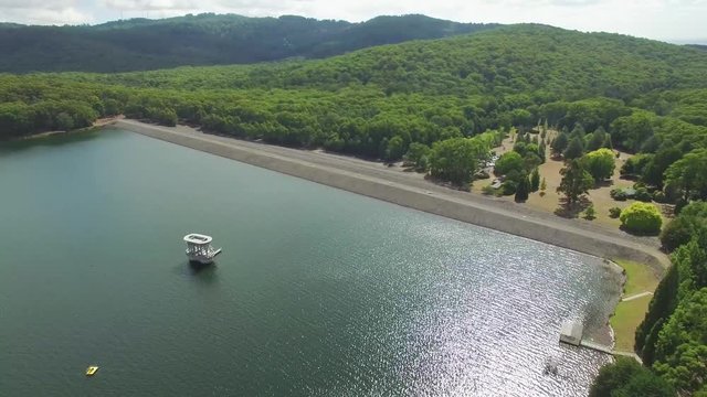 Forward flight over water reservoir lake dam wall and forest on sunny day