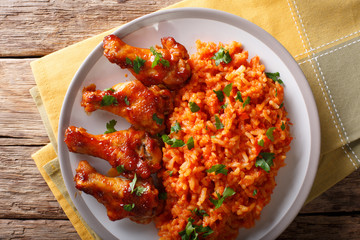 Porcion of African Jollof rice with fried chicken wings close-up on a plate. Horizontal top view