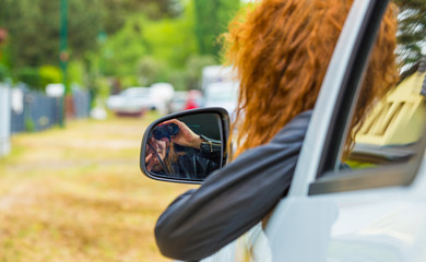 eine rothaarige Frau sitzt in einem Auto und beobachtet mit einem Fernglas