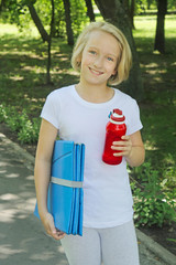Happy girl with a bottle of water and a mat for sports and yoga in the park