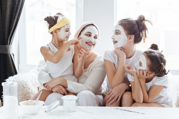 Mom with her daughters making clay face mask. Mother with children doing beauty treatment together. Morning skin care routine.