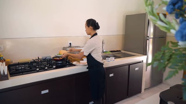 Balinese woman in black apron cooking breakfast at modern kitchen