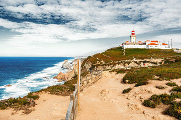 Fototapeta na wymiar Beautiful seascape. View from the cape of rock to the lighthouse over the Atlantic Ocean and two people standing in the distance on the cliff, Portugal. Sintra. Cape of rock.