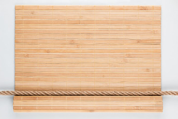 Naklejka na ściany i meble Bamboo mat with curled edges and rope, lying on a white background.