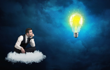 Fototapeta na wymiar Man sitting on cloud looking at a lightbulb