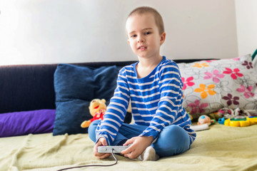 Cute boy playing video game console while sitting on sofa at home. Smiling and feeling happy