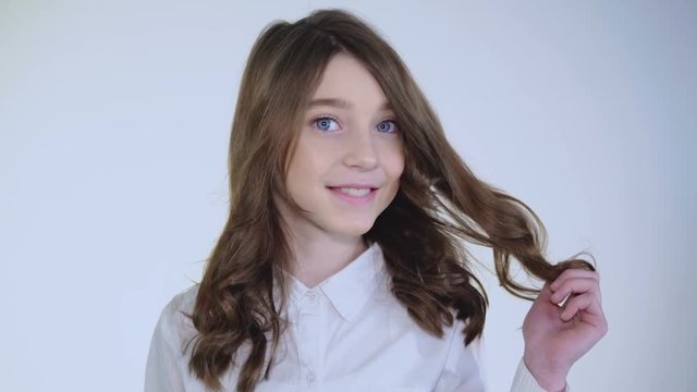 Young pretty modest girl plays her hair and smiles at camera