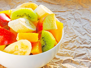 Fototapeta na wymiar Fresh juicy fruit salad in a white bowl on a background of crumpled paper