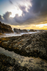 Ocean and rocky coastline against cloudy sky at sunrise