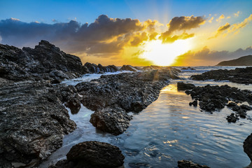 Ocean and rocky coastline against cloudy sky at sunrise