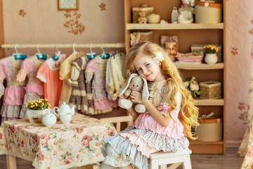 portrait of a romantic baby with long blond hair in a beautiful pink vintage dress with a plush Bunny sitting on a chair and posing for the camera.Little lady.Provence style