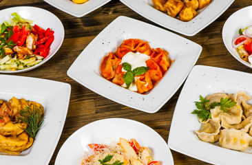 Set of different salads, dumplings and ravioli on a wooden table