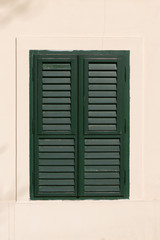 Closed old window with green wooden shutters on beige wall