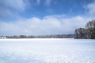 Fototapeta na wymiar Winter landscape with snow field in countryside and trees and hills on horizon