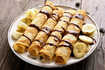 Delicious crepe roll with banana slices and chocolate sauce