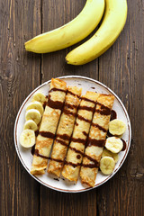 Delicious crepe roll with banana slices and chocolate sauce