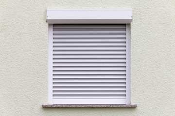 geschlossenes Fenster mit Rollo an einer weißen Wand