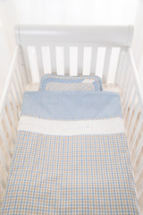Cozy baby cot with white square pillows and patchwork comforter blanket with stars and black stripes