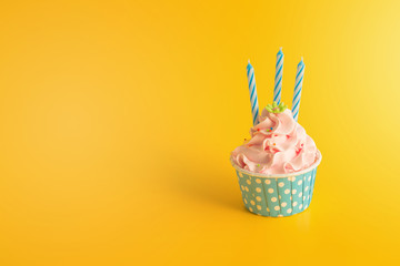 Tasty Birthday cupcake with candles on yellow color background