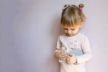 A serious little girl. A little girl with blond hair holds two wooden white hearts in her hands. It is thoughtful and serious.