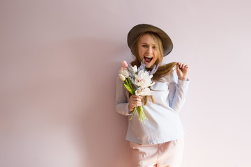 A young beautiful girl with blond dissolved long hair, a felt hat on her head, keeps spring flowers in her hands on a sunny day. Women's Day.