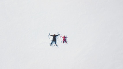 Child girl playing and making a snow angel in the snow with her mother . Top flat overhead view