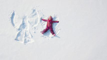 Child girl playing and making a snow angel in the snow. Top flat overhead view