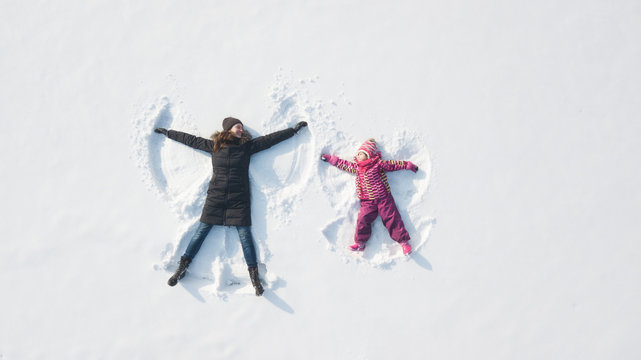 Child girl with mother playing and making a snow angel in the snow. Top flat overhead view