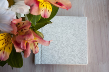 White notebook or album for photowoth place for text  is on the table in the morning with flowers on the side
