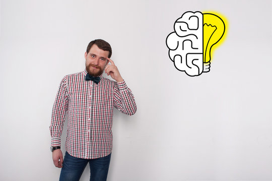 Young bearded caucasian man hipster pointing to his head and drawing of brain and lightbulb. Eureka and solving problem conept. Studio with white background and copyspace