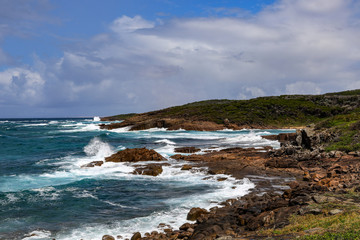 Waves crashing over rocky coastline with cloudy sky