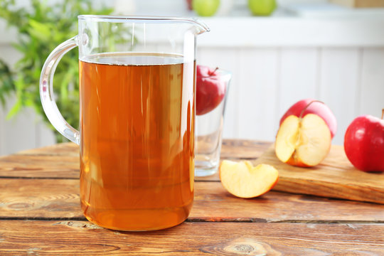 Jug with fresh apple juice on wooden table