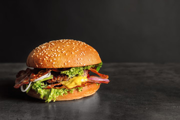 Tasty burger with bacon on dark background