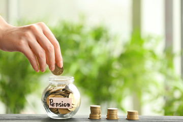 Hand putting coin into glass jar against blurred background. Pension planning concept