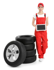 Female mechanic in uniform with car tires and tablet computer on white background