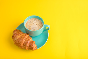 Bright blue plate and a cup of coffee (cocoa) stand on a cheerful yellow background tablecloth. A festive playful mood. Croissant dessert sweets for breakfast. Happy morning colors