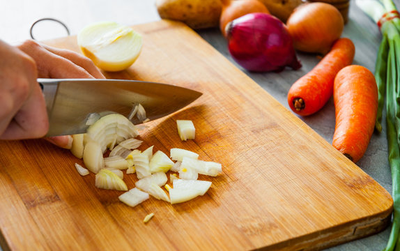 Chefs hands with knife chopping vegetables on wooden board