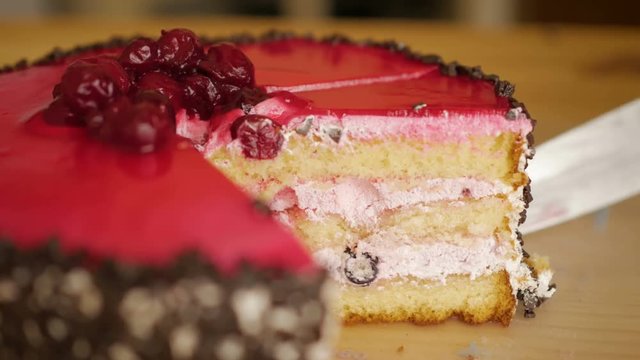 Person cutting a brown cake with a knife close up. Red cherry topping on chocolate cake. Pink icing on the pie. Closeup. 4K UHD