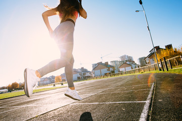 Female runner legs in shoes jogging on stadium track, back view, woman athlete running and working...