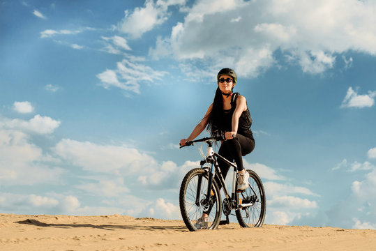 Full length image of young female cyclist looking forward. Fit sport woman wearing sportswear sitting on her bicycle. Extreme games. Desert trip.