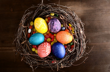 Easter painted eggs in the nest on wooden brown background top view