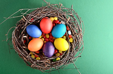 Easter painted eggs with candies in the nest on green background top view