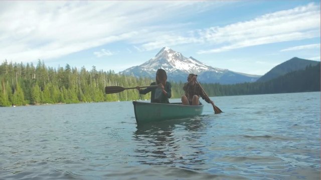 Young loving couple rowing a boat together with some paddles towards the shore on a lake