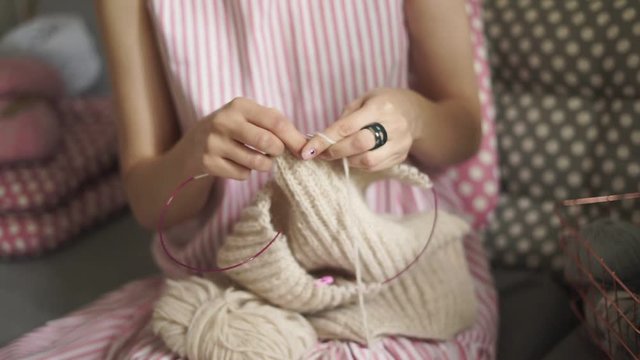 Close up female knitting hands. Woman knitting woolen sweater sitting on couch