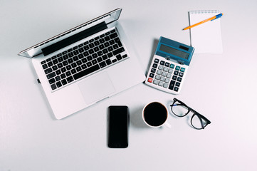 Work space table with laptop, phone, calculator, eyeglasses and coffee on grey background. Top...