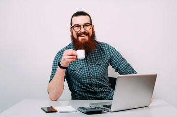 Portrait of cheerful smiling young man sitting at the table in front of laptop and drinking coffee Attractive business man looking at laptop computer screen expression
