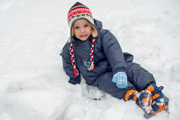 Little boy sitting in snow and playing