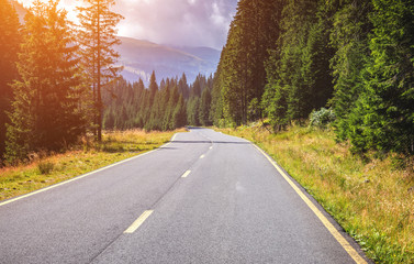 Fototapeta premium Mountain road. Landscape with rocks, sunny sky with clouds and beautiful asphalt road in the evening in summer. Vintage toning. Travel background. Highway in mountains. Transportation