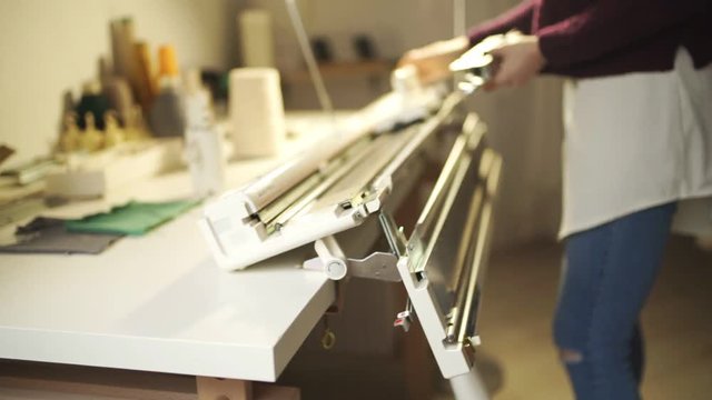 Young woman adjust knitting machine for working in home workshop. Craft woman working with knitting machine on table in textile workshop