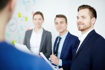 Fototapeta premium Young employee listening to one of colleagues opinion during discussion of working moments at start-up meeting